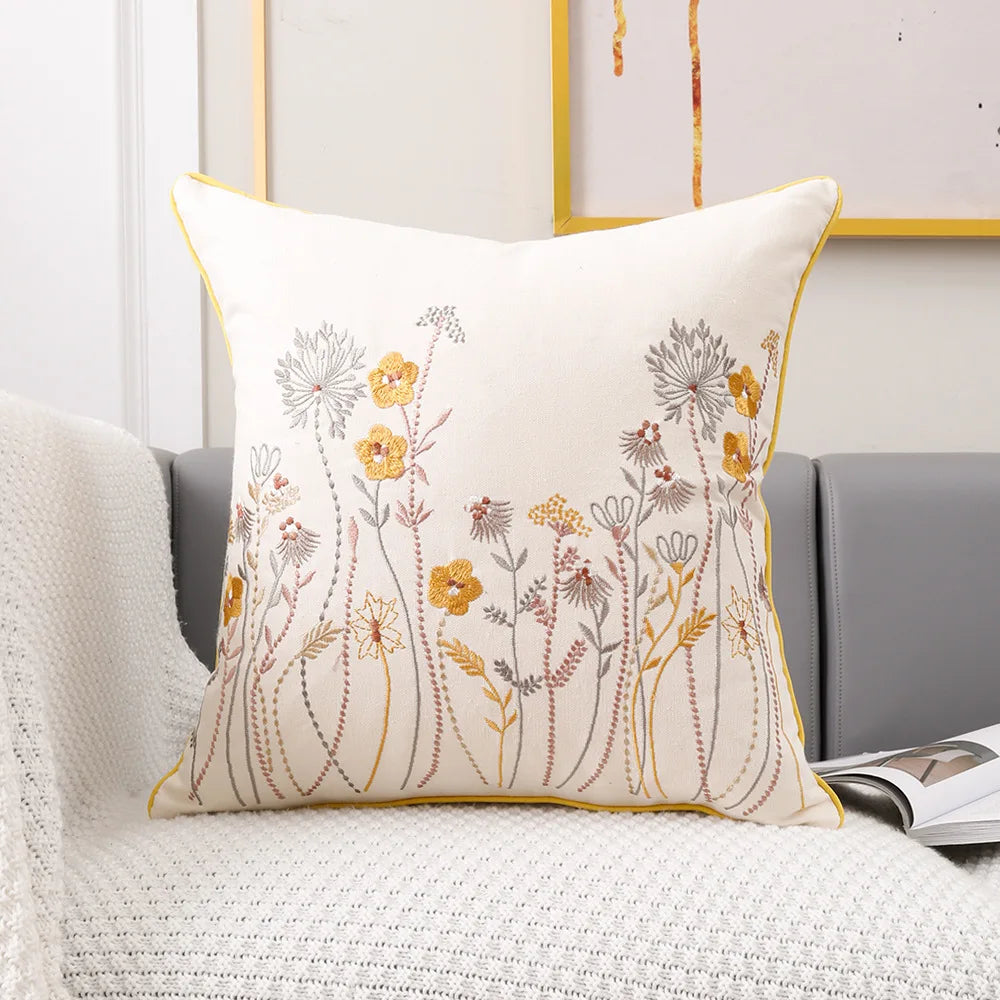 Coussin décoratif avec un motif floral élégant composé de fleurs et de feuillages brodés en couleurs chaudes sur un fond clair.