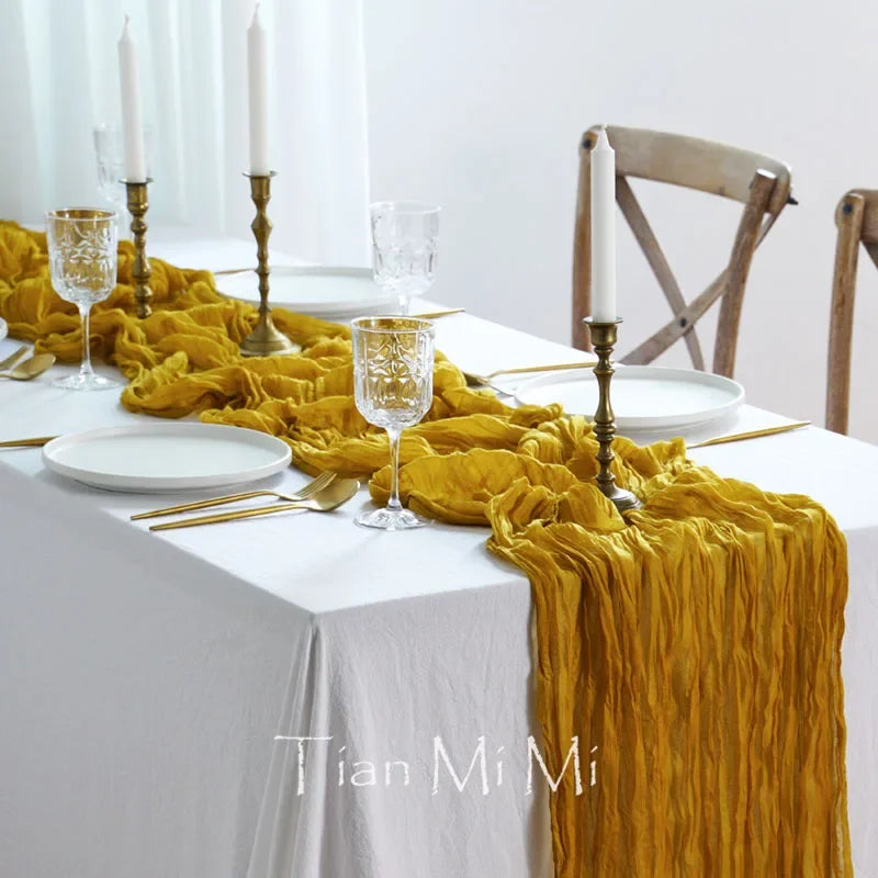 La table est dressée avec une nappe blanche, une chemin de table jaune froissé, des chandelles allumées, des verres de cristal et des assiettes blanches, créant une ambiance élégante et chaleureuse.
