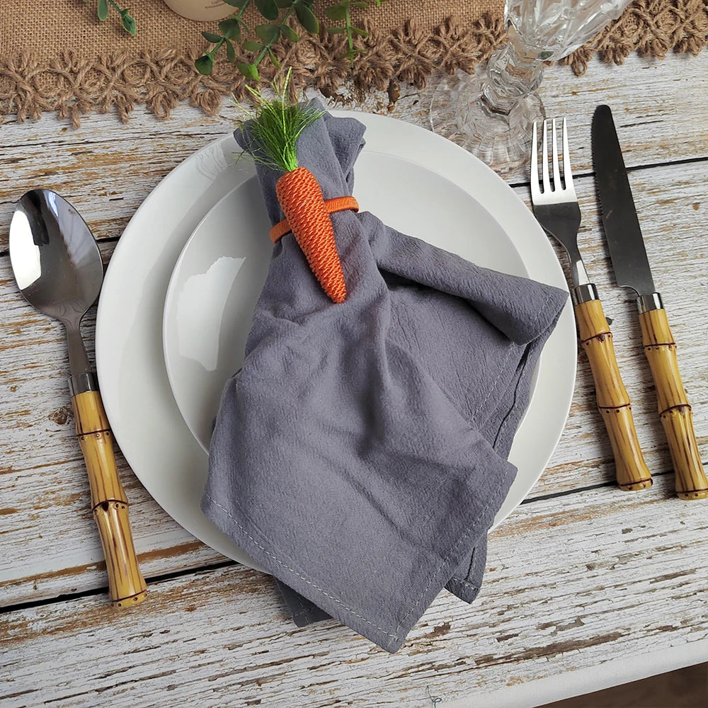 Une belle composition de table avec une serviette grise nouée autour d'une carotte en décoration, accompagnée d'une fourchette et d'un couteau en bambou sur un fond de bois rustique.