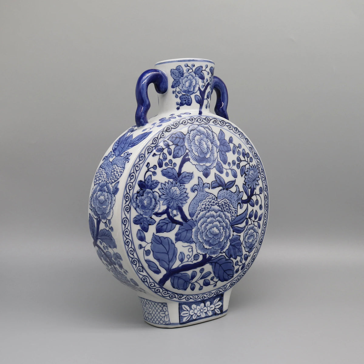 Vase en céramique orné de motifs floraux bleus et blancs, présentant une forme ronde et des anses latérales.