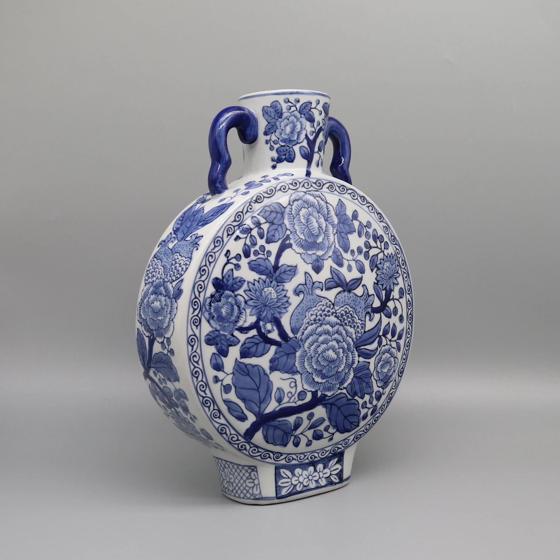 Vase en céramique orné de motifs floraux bleus et blancs, présentant une forme ronde et des anses latérales.