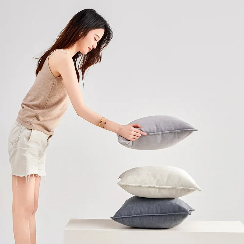 Une jeune femme souriante arrange élégamment des oreillers gris et blancs sur un support blanc.