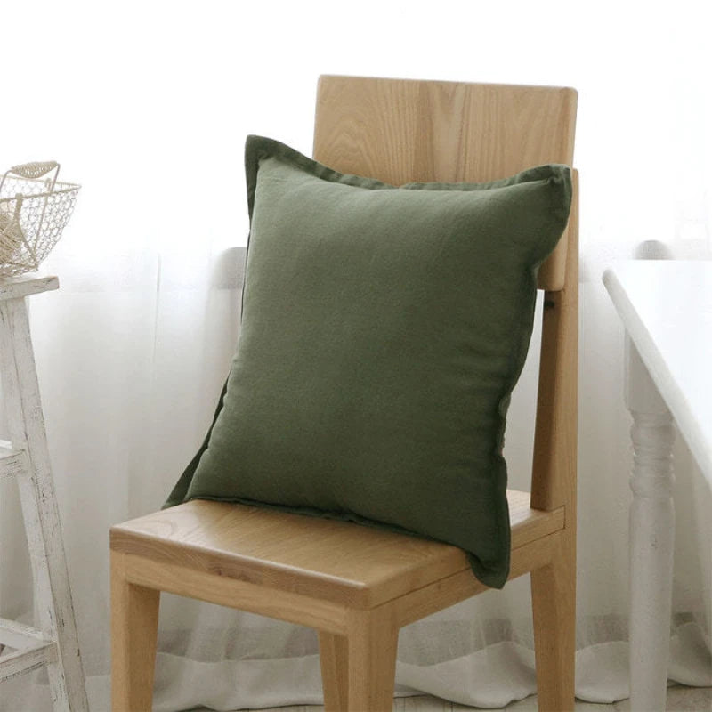 Coussin décoratif vert olive posé sur une chaise en bois, créant une atmosphère chaleureuse et apaisante dans l'espace.