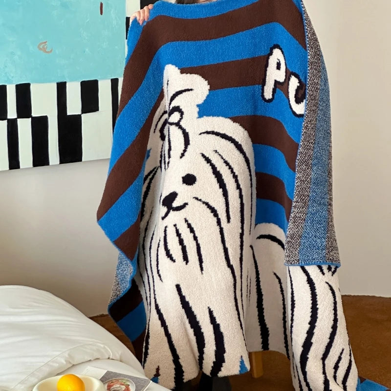 Une couverture en laine rayée de couleurs bleue et brune avec une représentation stylisée d'un chien blanc sur un fond texturé.