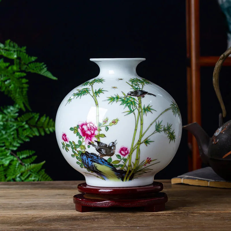 Un vase en porcelaine blanche décoré d'un motif de bambous, de fleurs et d'oiseaux colorés, disposé sur un présentoir en bois.