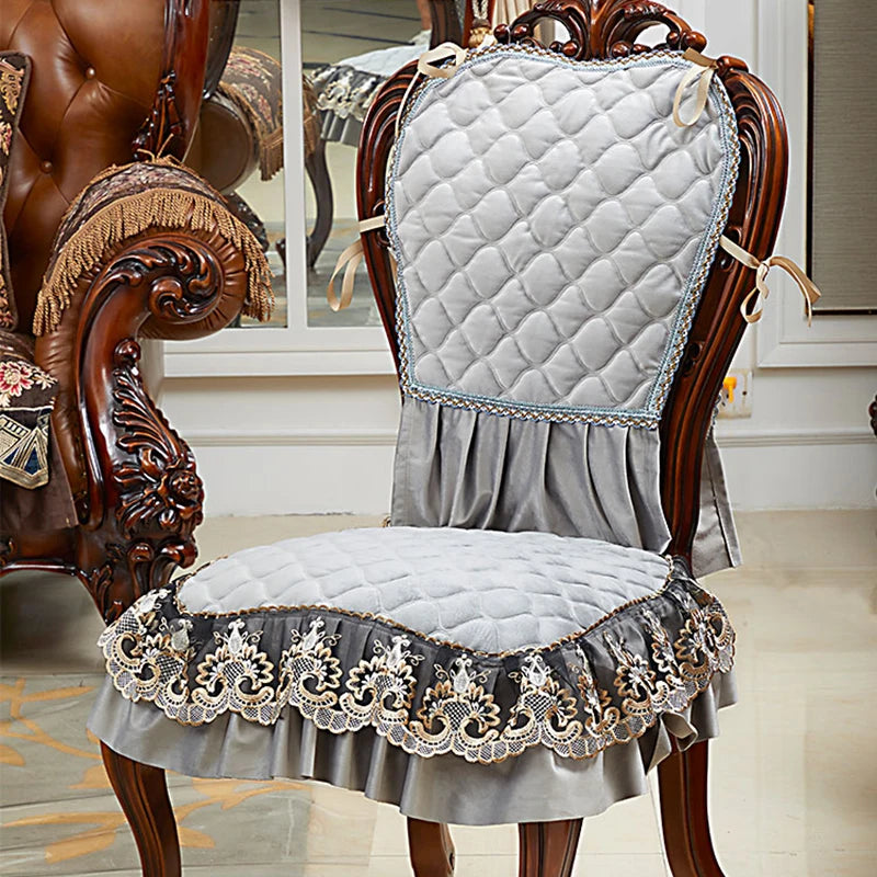 Cette image montre un fauteuil vintage en bois sculpté avec un rembourrage gris matelassé et une bordure en dentelle élégante, créant un style traditionnel et raffiné.