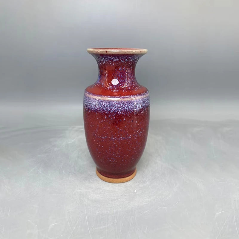 Vase en céramique de couleur rouge foncé avec des taches et des nuances de violet, avec un col étroit et une base large.