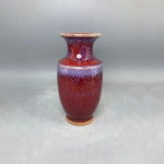 Vase en céramique de couleur rouge foncé avec des taches et des nuances de violet, avec un col étroit et une base large.