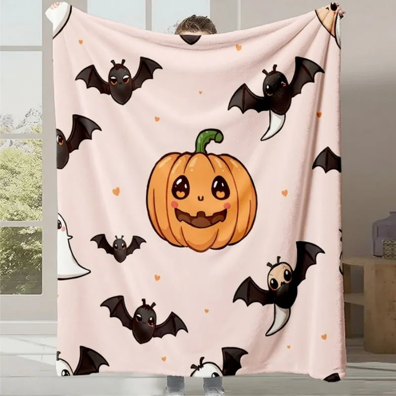 Couverture douce avec des motifs d'Halloween, comportant une citrouille souriante et des chauves-souris noires sur un fond rose clair.