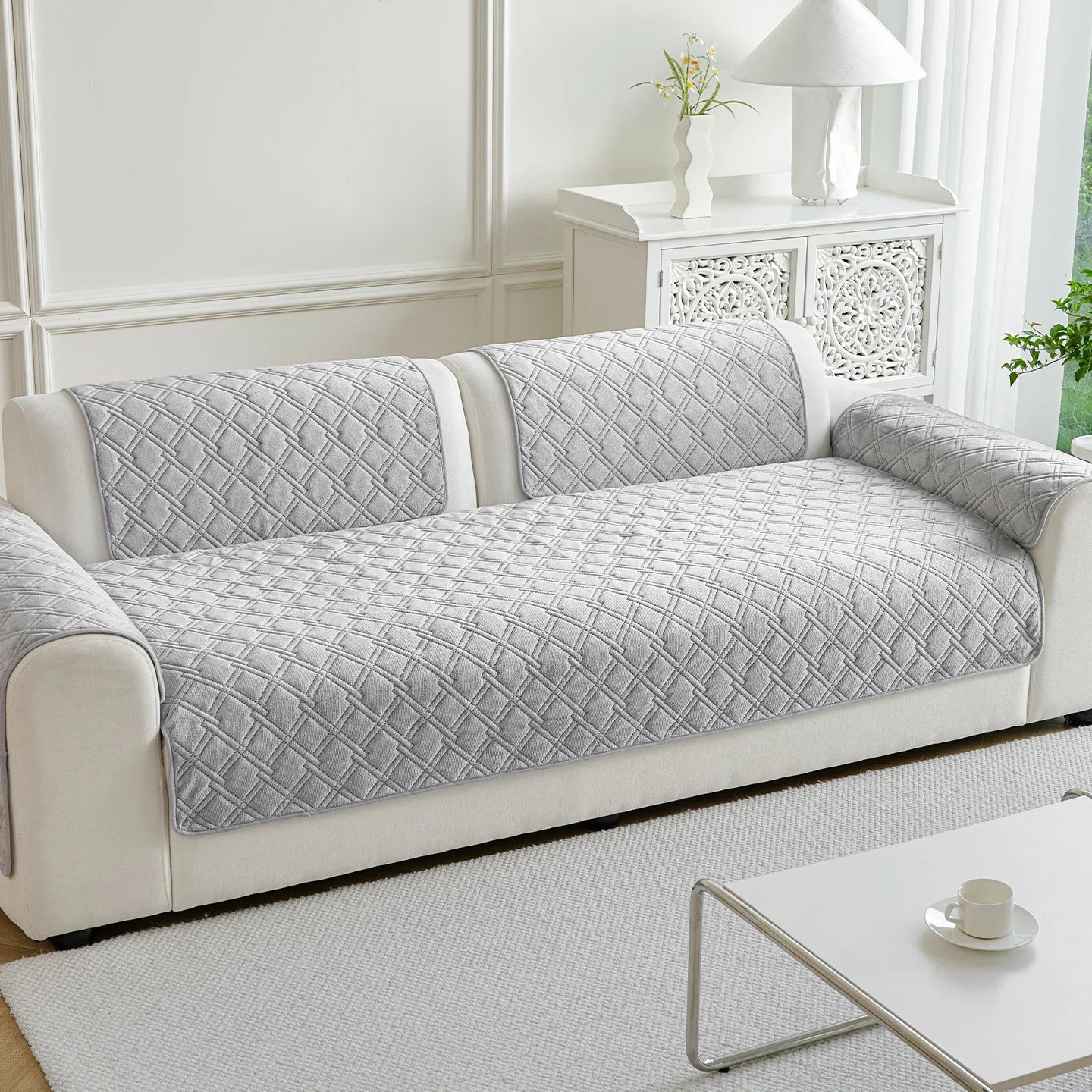 Canapé gris aux motifs géométriques élégants, placé dans un salon lumineux et épuré, complété par un meuble décoratif blanc.