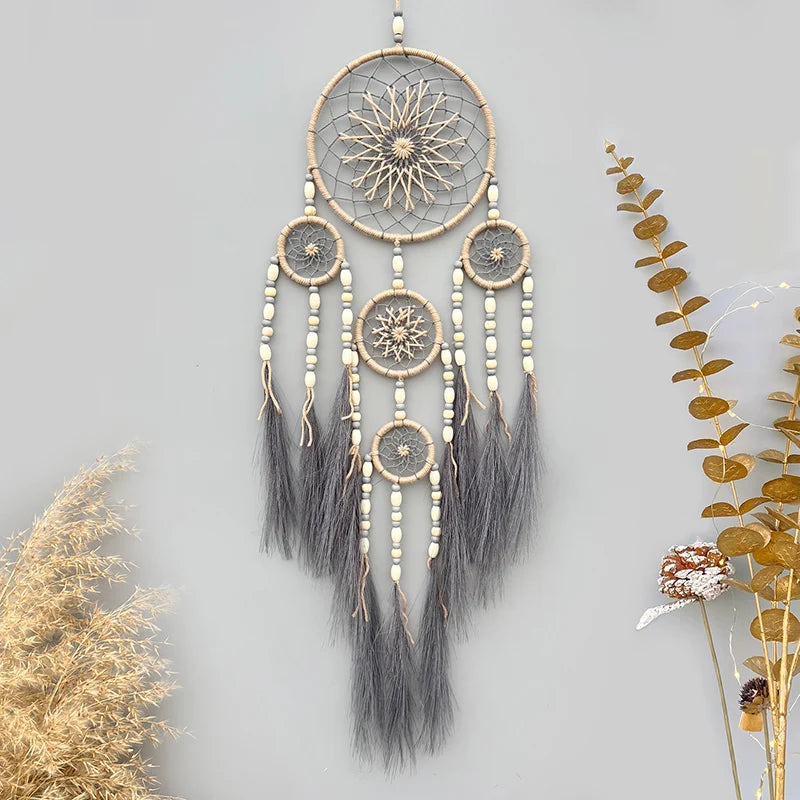 Un magnifique attrape-rêves en macramé avec des perles blanches et des plumes grises ornant un encadrement rond décoré de motifs floraux, suspendu contre un mur gris aux touches de verdure.