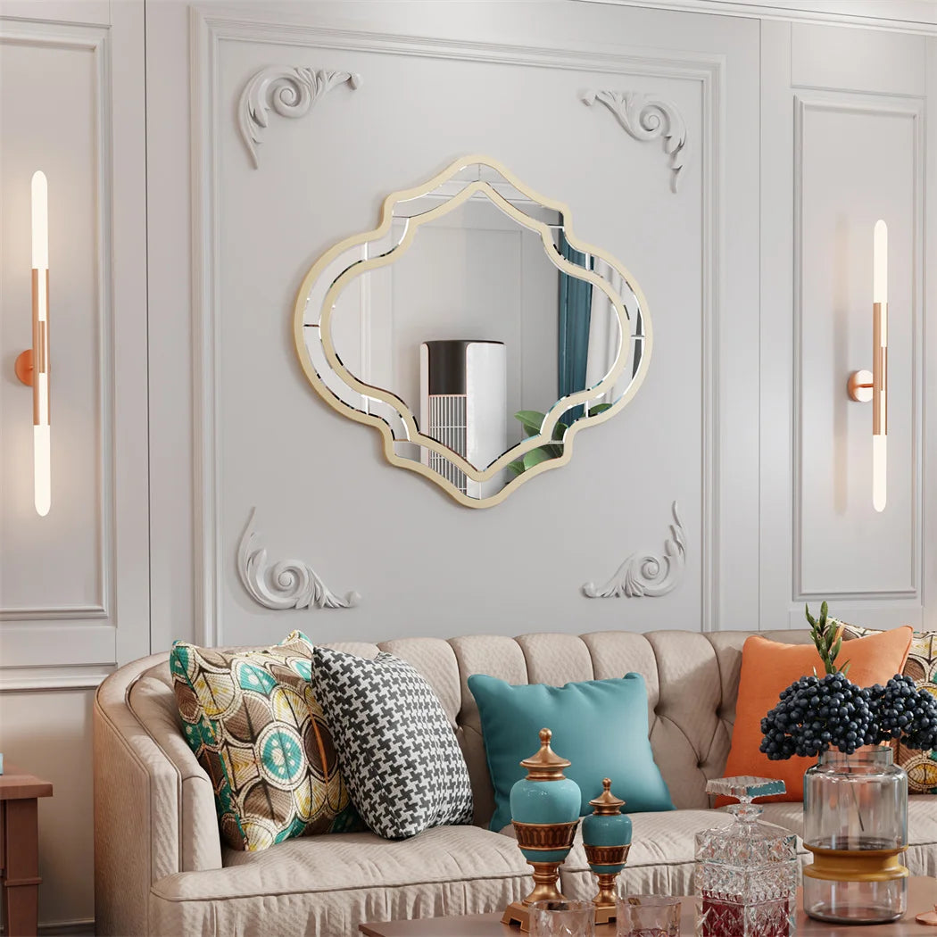 Le salon présente une décoration élégante avec un canapé capitonné beige, des coussins colorés et un miroir ornemental au mur.