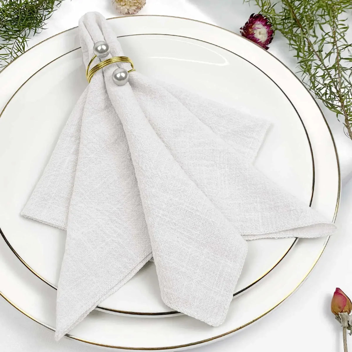 Serviettes blanches avec anneaux dorés sur une assiette blanche décorée de fleurs fraîches.