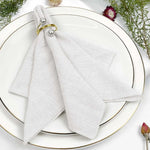 Serviettes blanches avec anneaux dorés sur une assiette blanche décorée de fleurs fraîches.