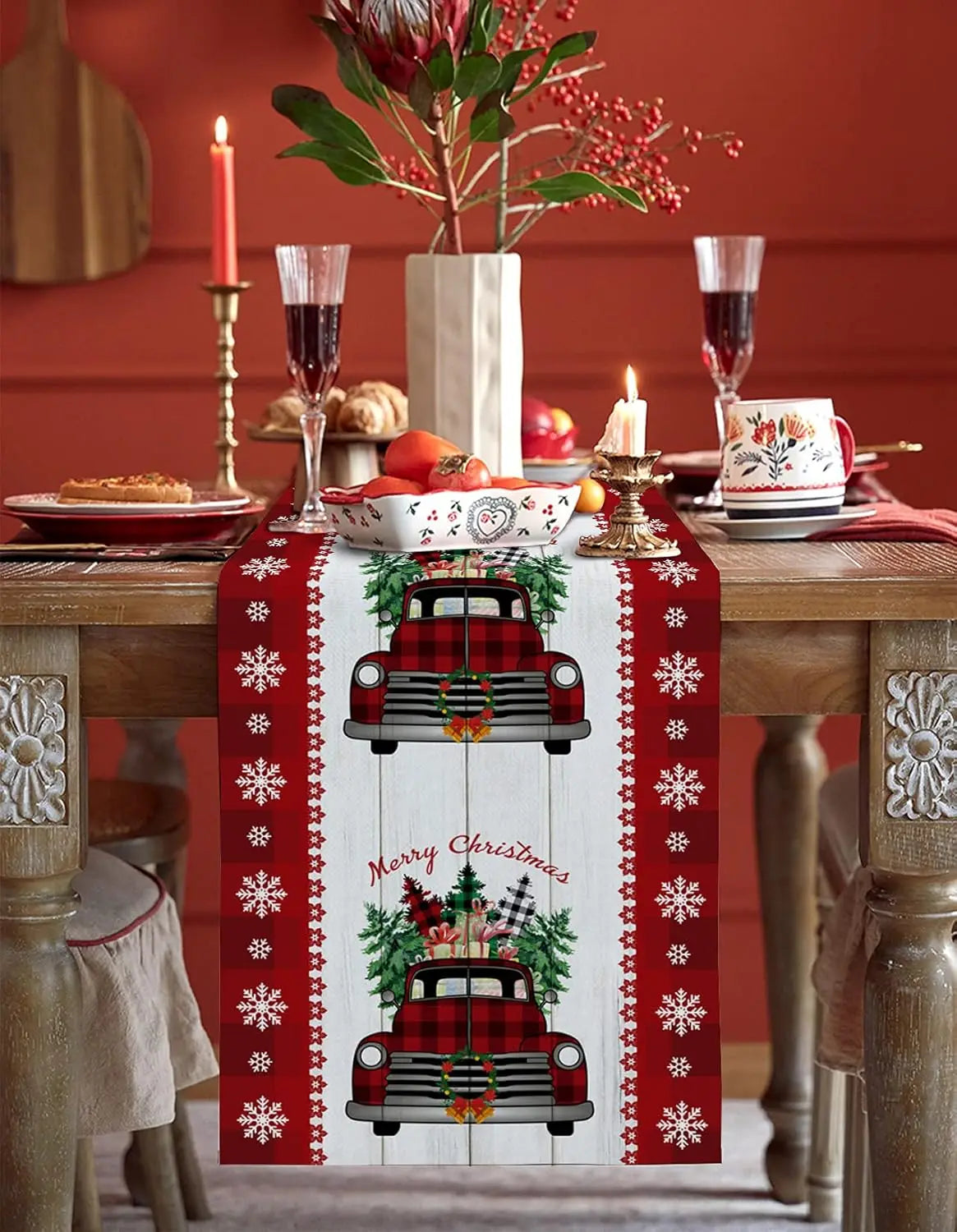 Décorations de table de Noël élégantes avec des éléments traditionnels tels que des bougies, un centre de table fleuri et un chemin de table en rouge et blanc avec des motifs de camions vintage.