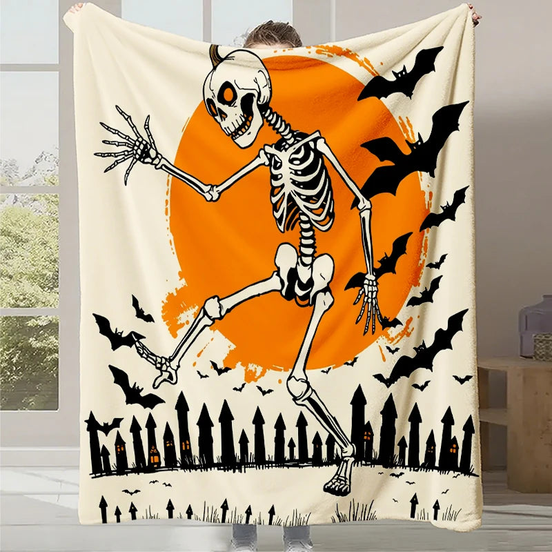 Une couverture en fleece blanche présentant un squelette dansant devant une lune orange et des silhouettes d'arbres noirs, avec des chauves-souris volant dans le ciel sombre.