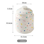Pot de rangement en céramique blanc à motifs multicolores, mesurant 10 cm de largeur, 12,6 cm de hauteur et avec une capacité d'environ 1000 ml.