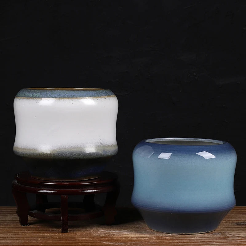 Deux pots en céramique colorés sur un support en bois dans un environnement sombre.