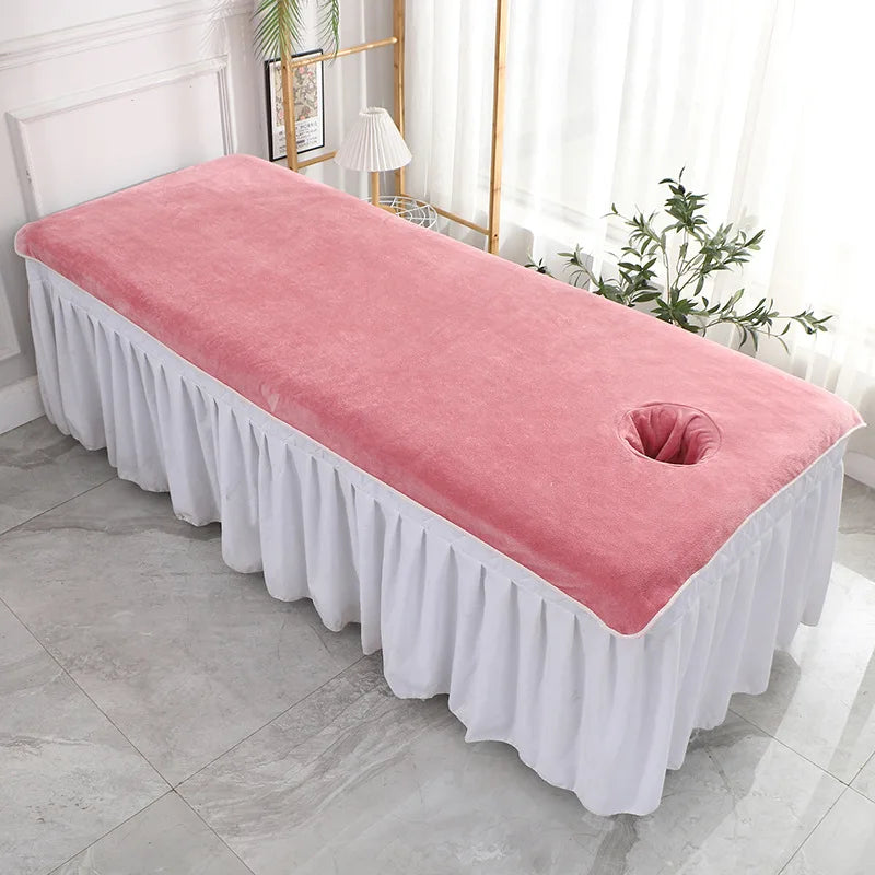 Une table de massage élégante et confortable avec un couvre-lit rose et une jupe blanche, placée dans une pièce lumineuse et moderne.