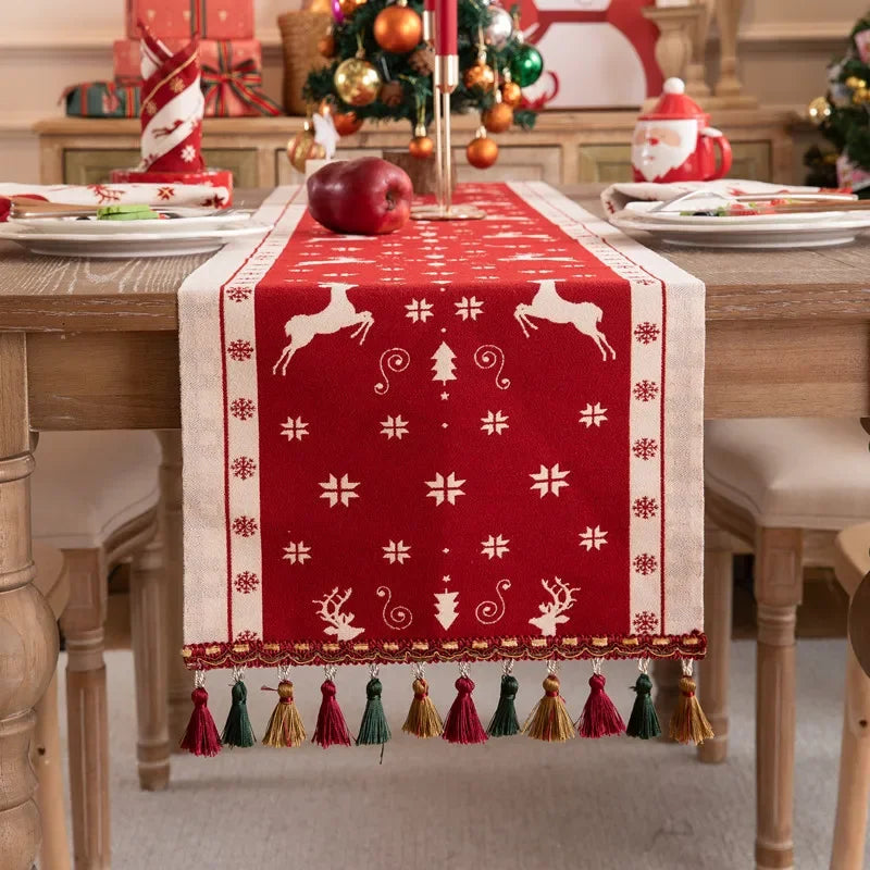 Décor de table de Noël avec un chemin de table rouge orné de motifs de rennes et de flocons de neige, de bougies et de décorations festives.