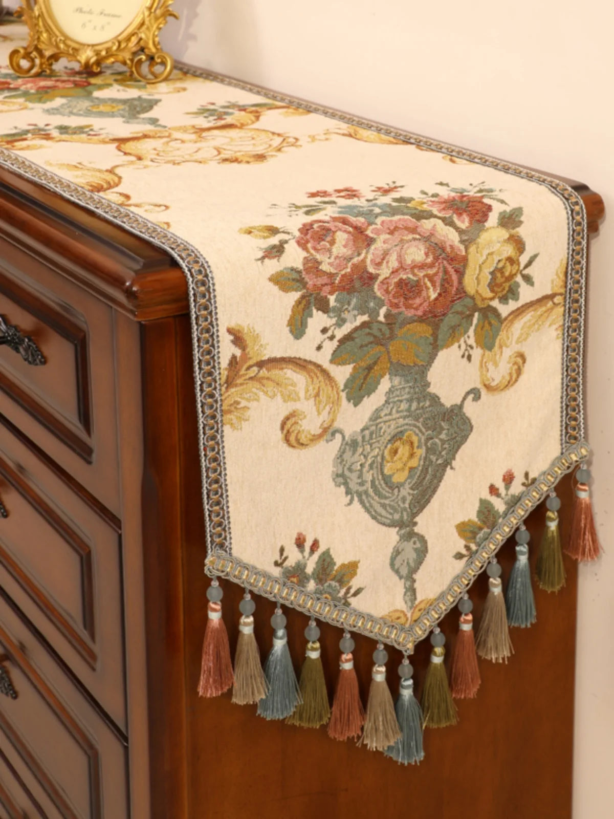Ce magnifique chemin de table orné de bouquets de fleurs colorés et d'une élégante frange à pompons ajoute une touche de raffinement vintage à ce meuble en bois.