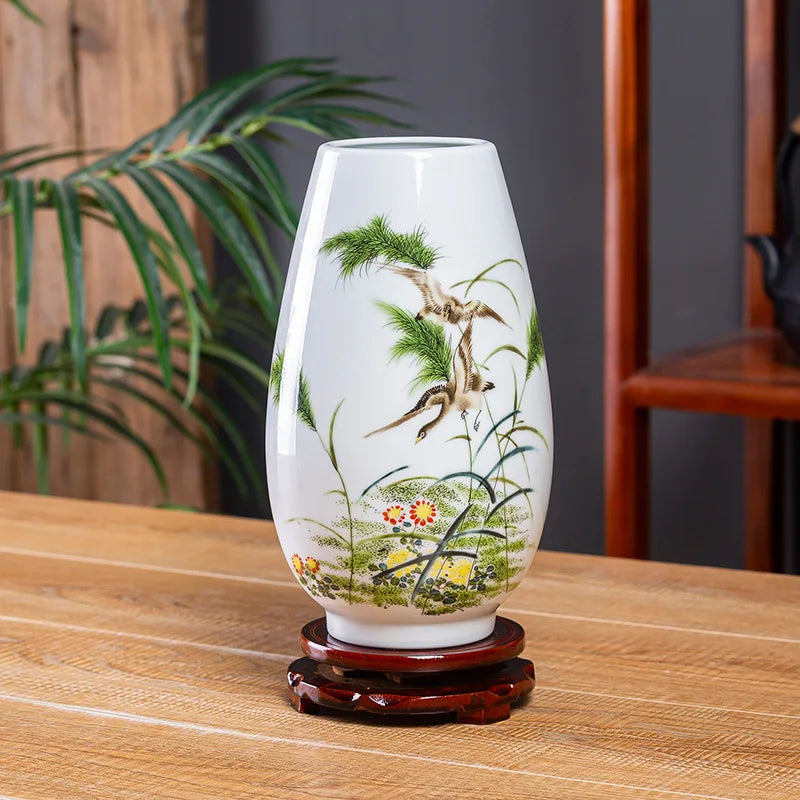 Un vase décoratif en porcelaine blanche avec une scène colorée d'une végétation luxuriante et d'un oiseau volant, posé sur un socle en bois.