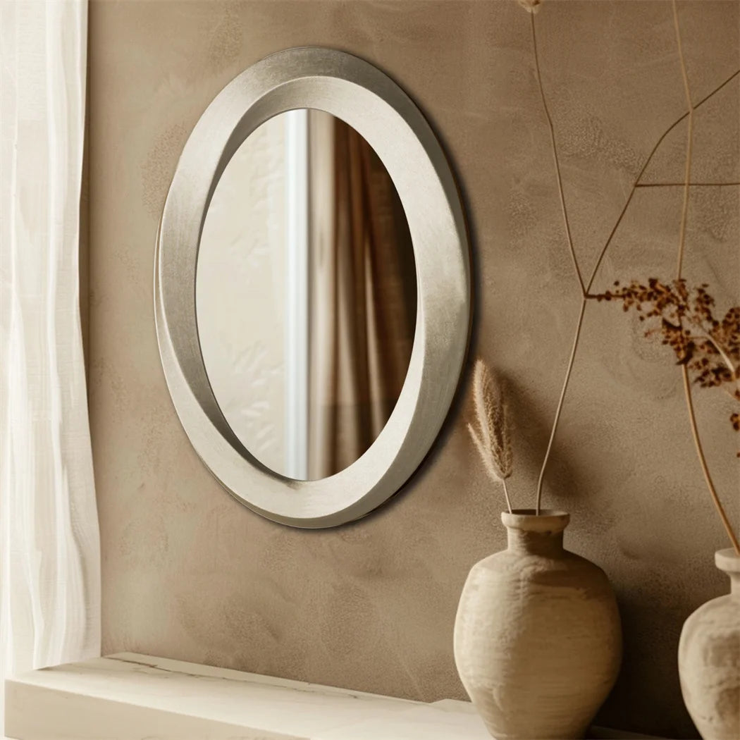 Un miroir ovale élégant suspendu sur un mur beige, accompagné d'un vase ornemental, reflétant une atmosphère paisible et épurée.