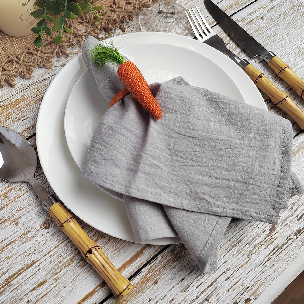 L'image montre une assiette blanche avec des ustensiles en bois, un linge gris décoré d'une carotte orange, et des accessoires de table sur un fond en bois.