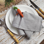 L'image montre une assiette blanche avec des ustensiles en bois, un linge gris décoré d'une carotte orange, et des accessoires de table sur un fond en bois.