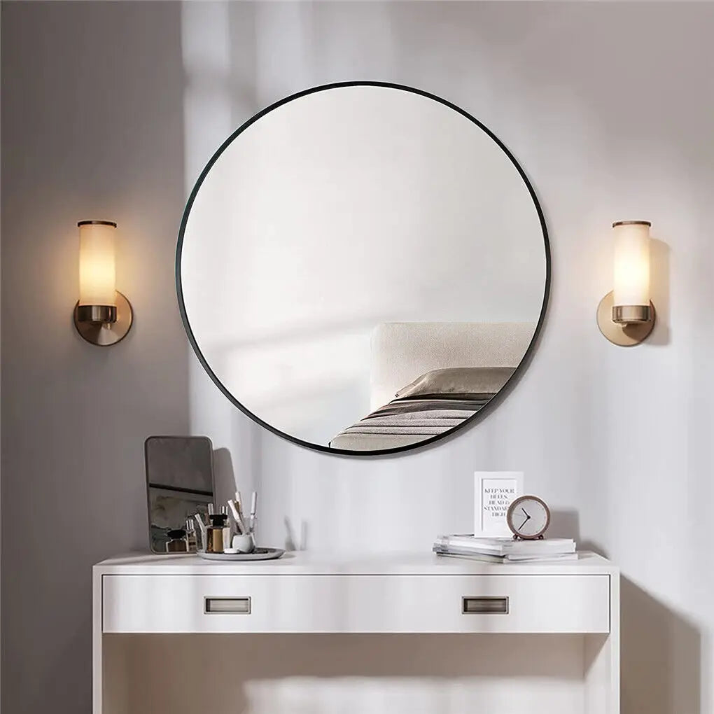 Une salle de bain élégante avec un miroir rond, des appliques murales et un meuble bas blanc avec des tiroirs.