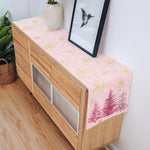 Cette image présente un meuble en bois avec un dessus recouvert d'un motif de flocons de neige et de sapins roses sur fond clair, décoré d'un vase et d'un cadre avec une silhouette d'oiseau.