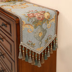Un magnifique chemin de table brodé de motifs floraux colorés, agrémenté de franges et de perles, qui apporte une touche de raffinement et d'élégance à ce meuble en bois.