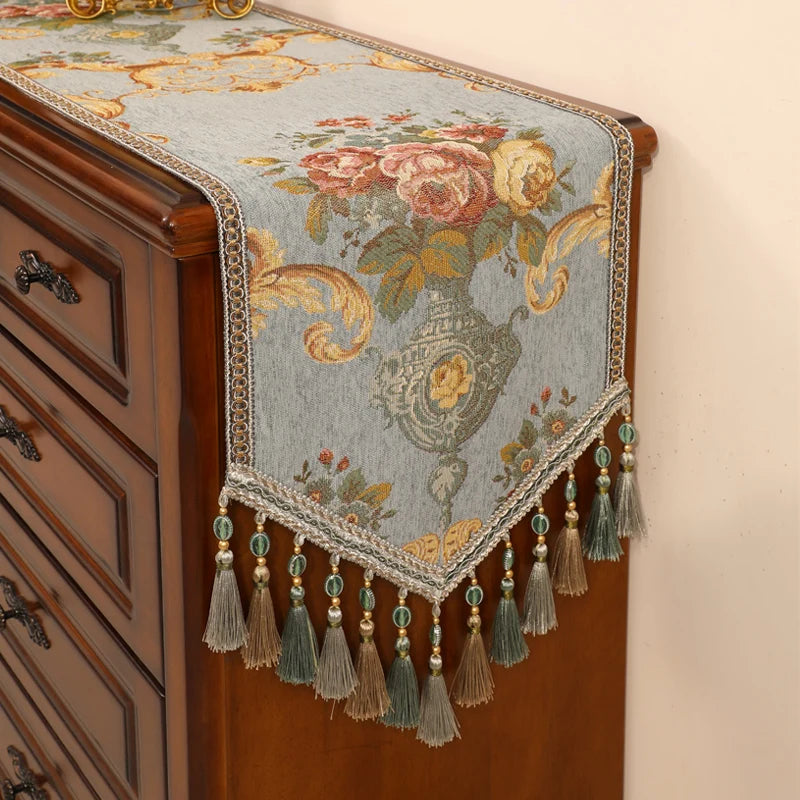 Un magnifique chemin de table brodé de motifs floraux colorés, agrémenté de franges et de perles, qui apporte une touche de raffinement et d'élégance à ce meuble en bois.