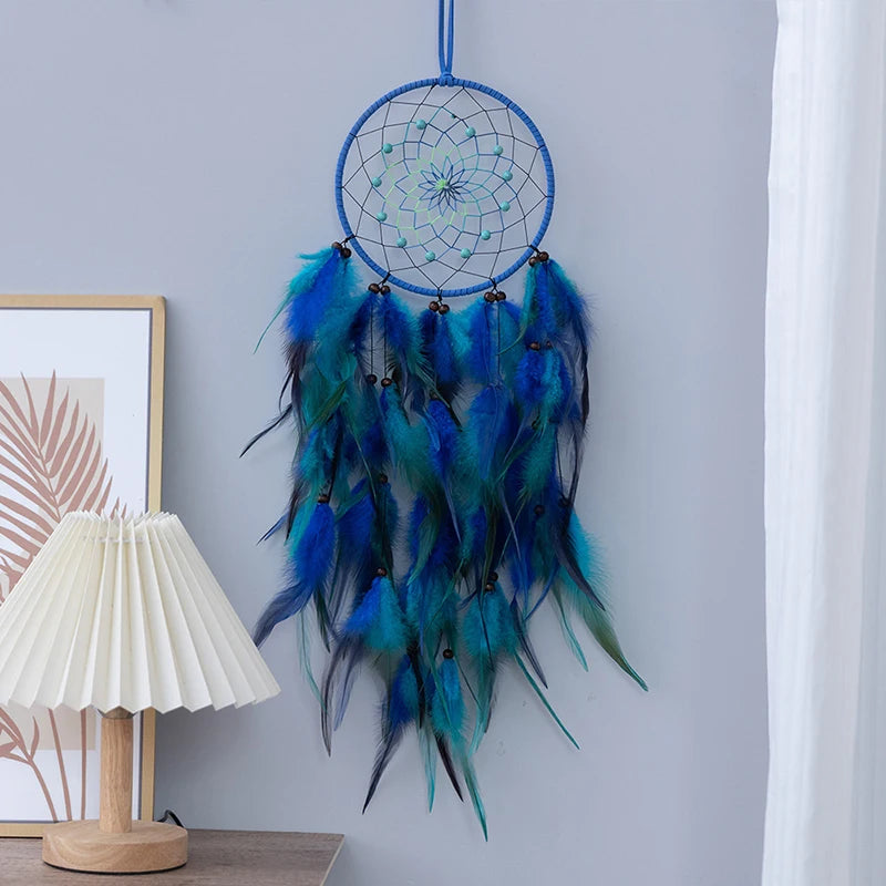 Un magnifique attrape-rêves bleu et vert orné de plumes de couleurs vibrantes, suspendu sur un mur blanc, avec une lampe en arrière-plan.