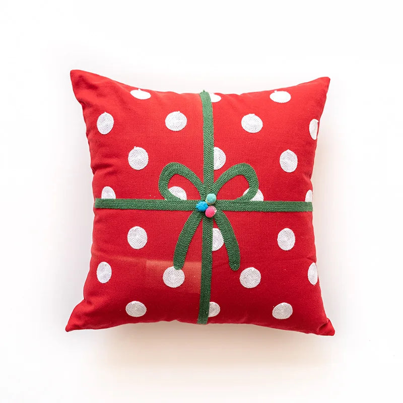 Coussin décoratif rouge à pois blancs avec un nœud vert et une fleur décorative.