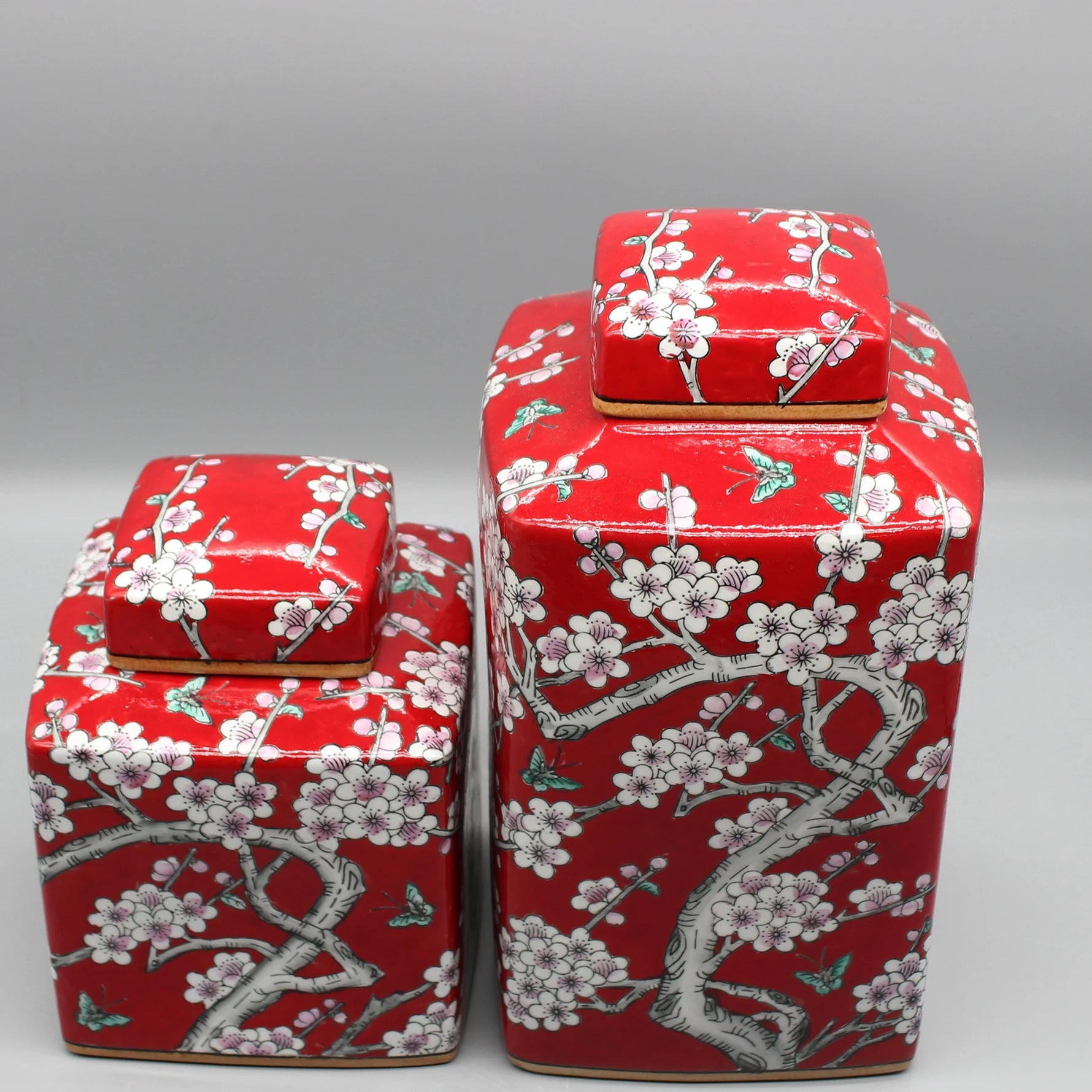 Des boîtes décoratives rouges ornées de motifs floraux blancs et gris, disposées en groupe sur un fond neutre.