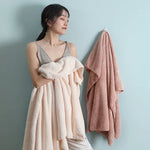 Une jeune femme portant une robe beige élégante, avec un châle rose posé sur le côté.