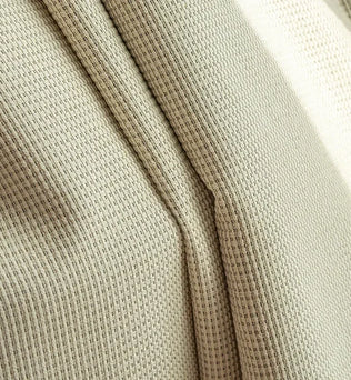 Gros plan sur un tissu beige avec un motif en maille serrée. Idéal pour la décoration intérieure ou la confection de vêtements modernes et élégants. Sa finition soignée et son design texturé apportent une touche de sophistication et de style à tout projet créatif.