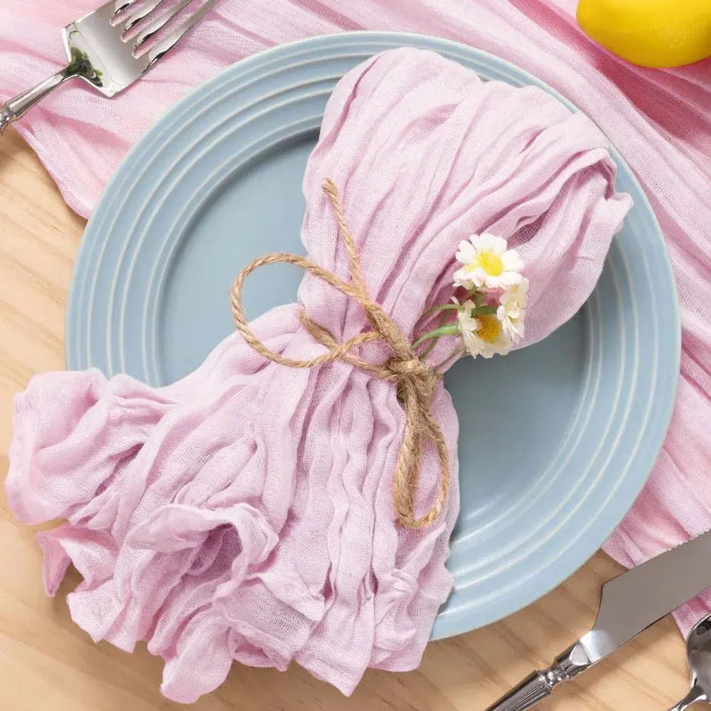 Une serviette rose froissée, joliment nouée avec de la ficelle de jute et agrémentée d'une petite fleur blanche, posée sur une assiette bleue sur une table en bois.