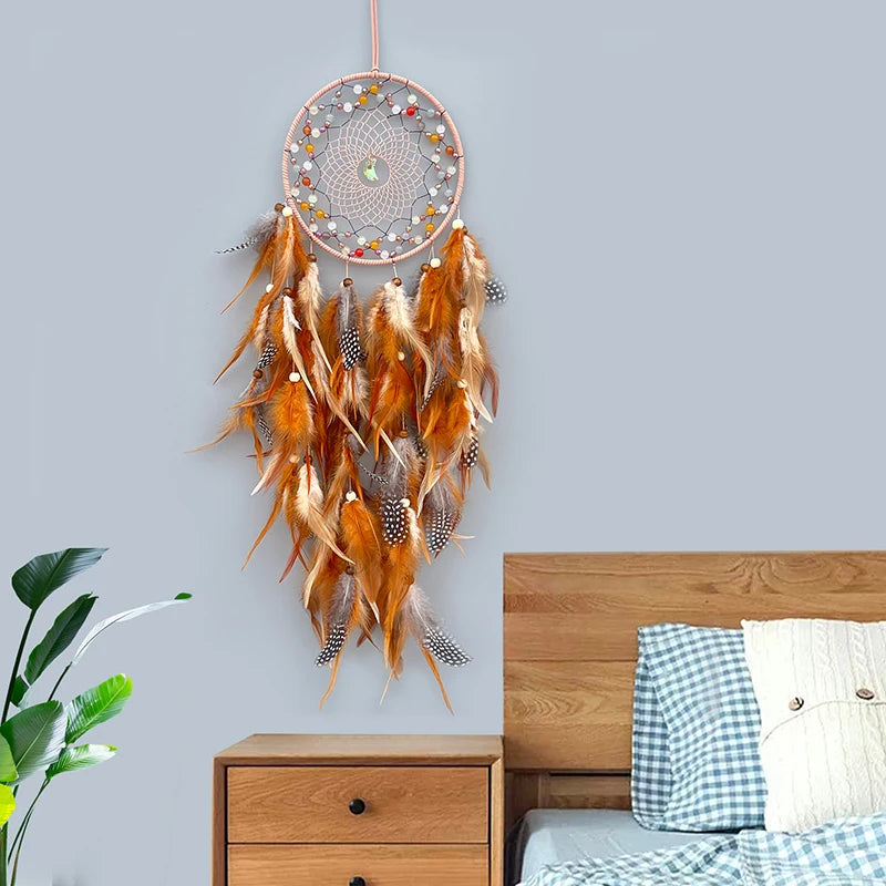 Capteur de rêves décoratif aux plumes oranges et noires, avec des pierres colorées, suspendu dans une chambre près d'un mobilier en bois.