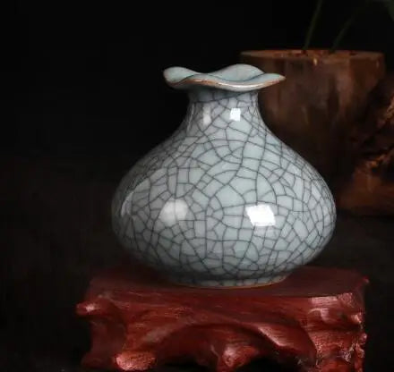 Vase en céramique antique décoré d'un motif craquelé bleuté sur un support en bois rougeâtre.