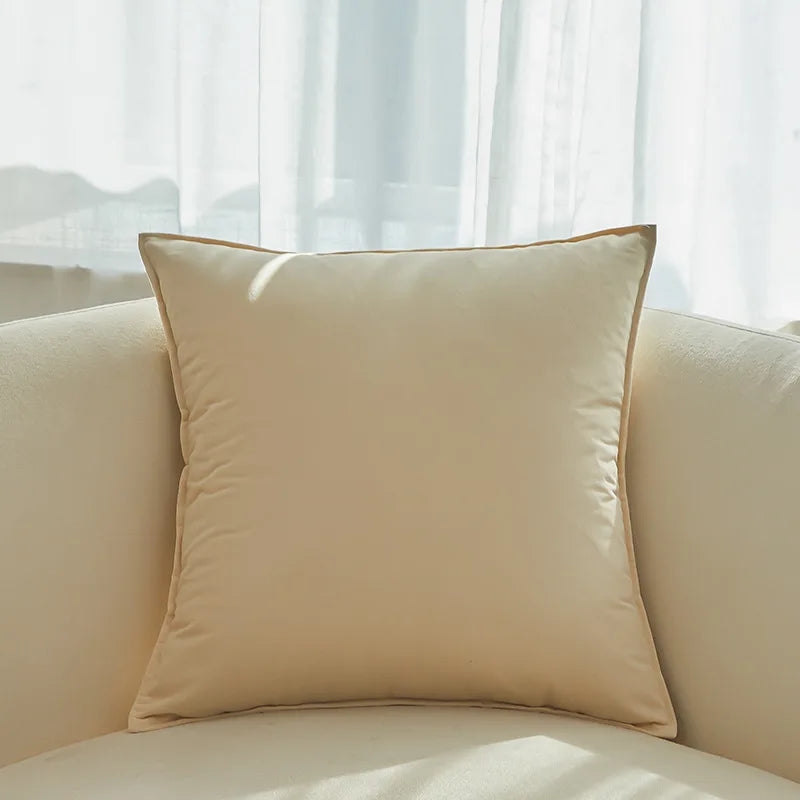 Un coussin décoratif beige élégant posé sur un canapé près d'une fenêtre donnant sur un paysage extérieur flou.