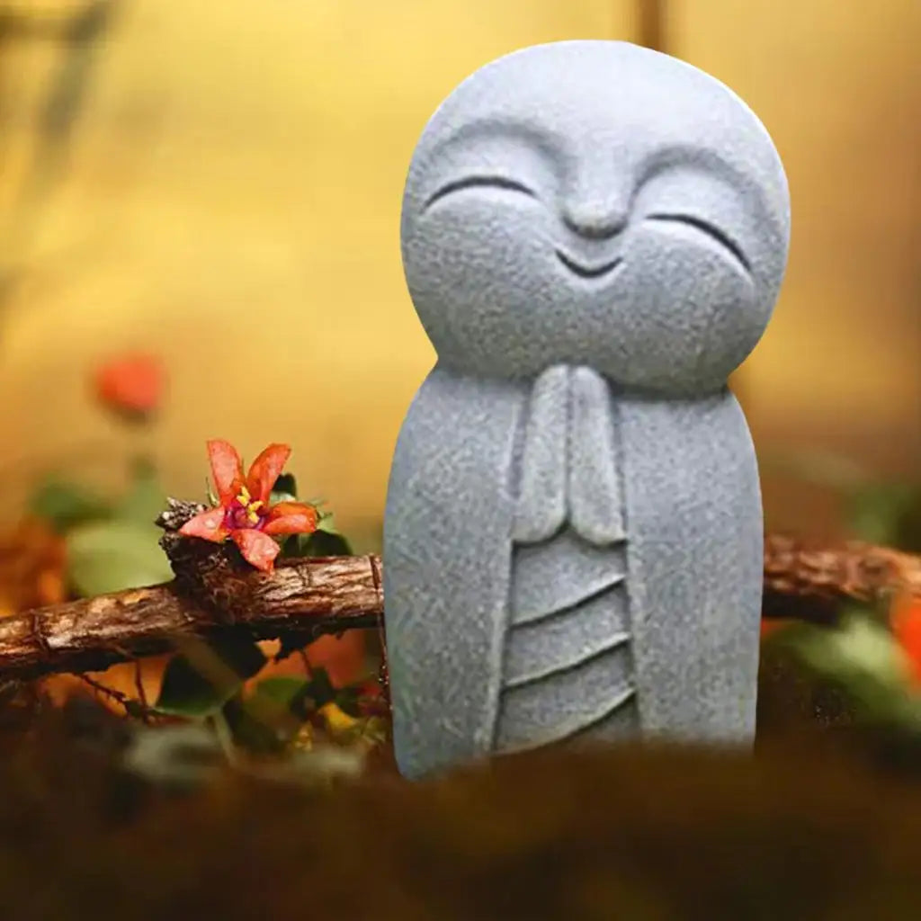 statue personnage yeux fermés sourire gris clair texture granuleuse plantes succulentes mousse fleurs zen
