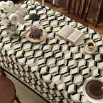 Sur la table se trouve un beau gâteau, un livre ouvert, une tasse de café et un vase de fleurs blanches, posés sur un joli motif géométrique noir et blanc.