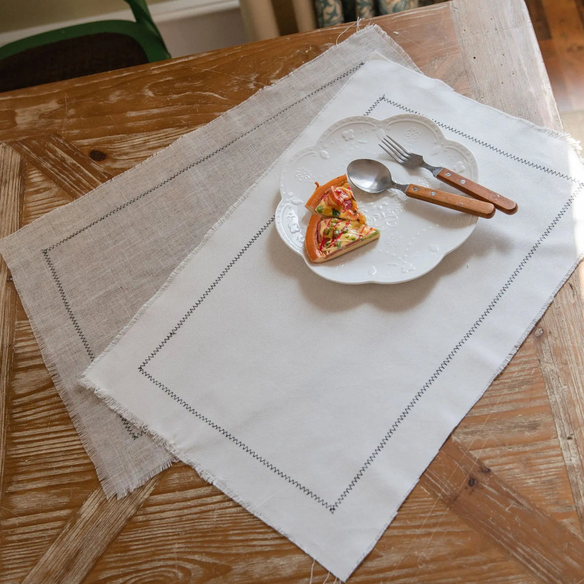 Une assiette blanche avec un morceau de pizza posé dessus, accompagné d'une fourchette et d'une cuillère en bois sur un linge de table beige.