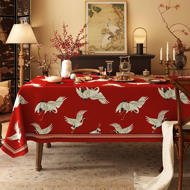 Élégante table dressée avec nappe rouge ornée de grues volantes, accompagnée d'un décor oriental sophistiqué dans un intérieur chaleureux et cosy.