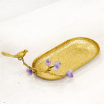 Un plat d'or délicat décoré de petits cristaux de quartz violet, surmonté d'un petit oiseau en métal doré.