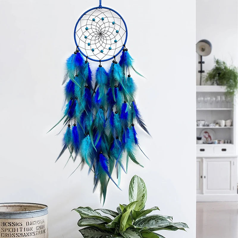 Un capteur de rêves bleu et vert suspendu, ornée de plumes colorées, est placé à côté d'une plante verte dans un intérieur moderne.