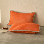 Deux oreillers moelleux de couleur orange vif, posés sur un fond clair, créent une ambiance chaleureuse et contemporaine.