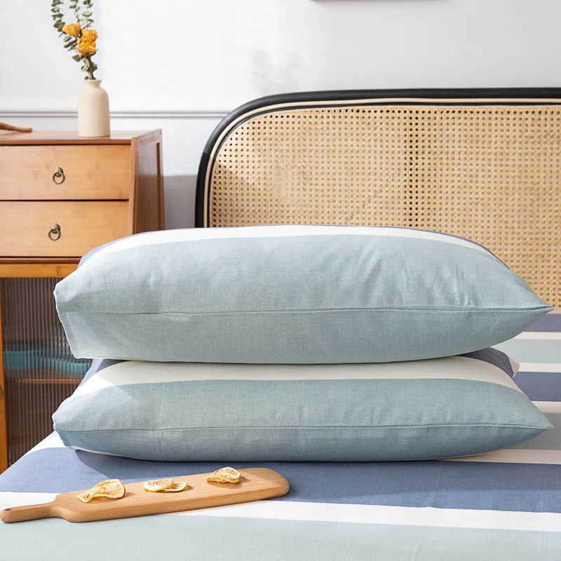 Deux oreillers moelleux gris menthe posés sur un lit, près d'un meuble en bois vintage et d'un arrangement floral, créant une ambiance apaisante dans la chambre.